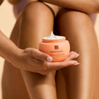 A person holding an open jar of Her Wisdom whipped body cream, with cream swirled on top.