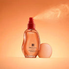 Her Wisdom Hydrating Skin & Hair Perfume Mist with a red spray top, shown spraying with mist visible, on a warm orange background.
