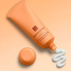 Avon Her Wisdom Baobab Intensely Restoring Wonderbalm tube in a peach-orange color, shown with its cap off and a squiggle of white balm beside it on a matching peach background.