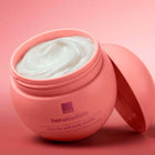 An open pink jar of Avon Her Wisdom Osmanthus The Flower of Mind velvety soft body souffle moisturised and conditioned sensitive skin cream, showing the white cream inside, with its matching pink lid leaning against it on a pink background.