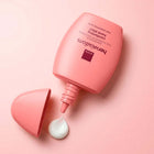 A pink Avon Her Wisdom Osmanthus hand elixir bottle with its cap off, showing a dollop of white cream below, set against a solid pink background.
