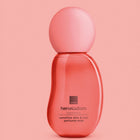 A bottle of Avon Her Wisdom Osmanthus sensitive skin & hair perfume mist in a translucent coral pink color, set against a solid pink background.